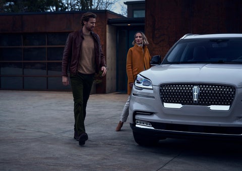 A man and a woman approaching a 2024 Lincoln Aviator® SUV, which illuminates certain lights when they are close | Baldwin Lincoln in Covington LA