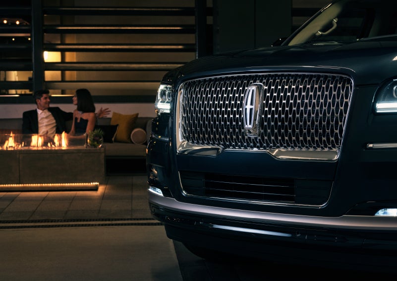 The signature Lincoln grille on the 2022 Lincoln Navigator SUV commands attention as a couple relaxes by a fire beyond | Baldwin Lincoln in Covington LA