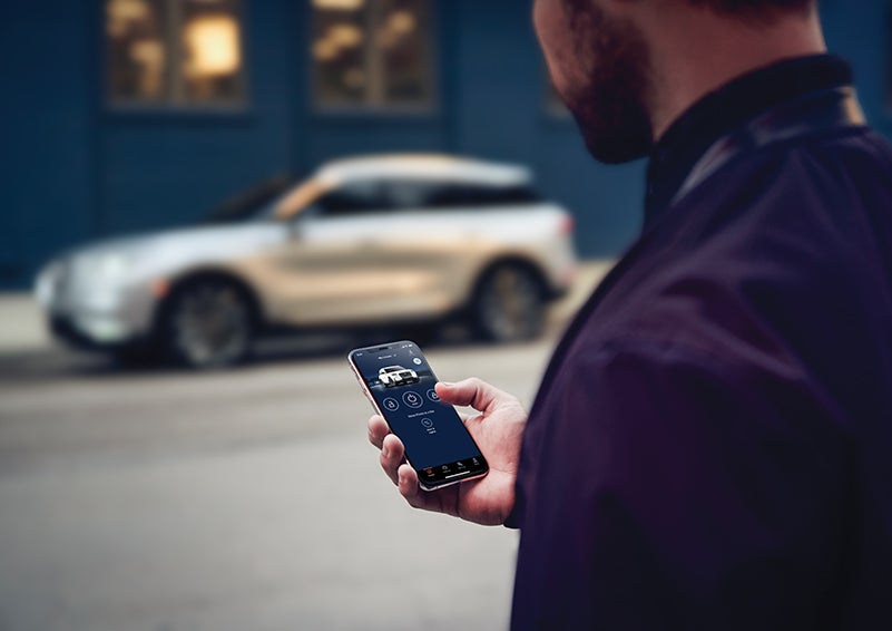 A person is shown interacting with a smartphone to connect to a Lincoln vehicle across the street. | Baldwin Lincoln in Covington LA